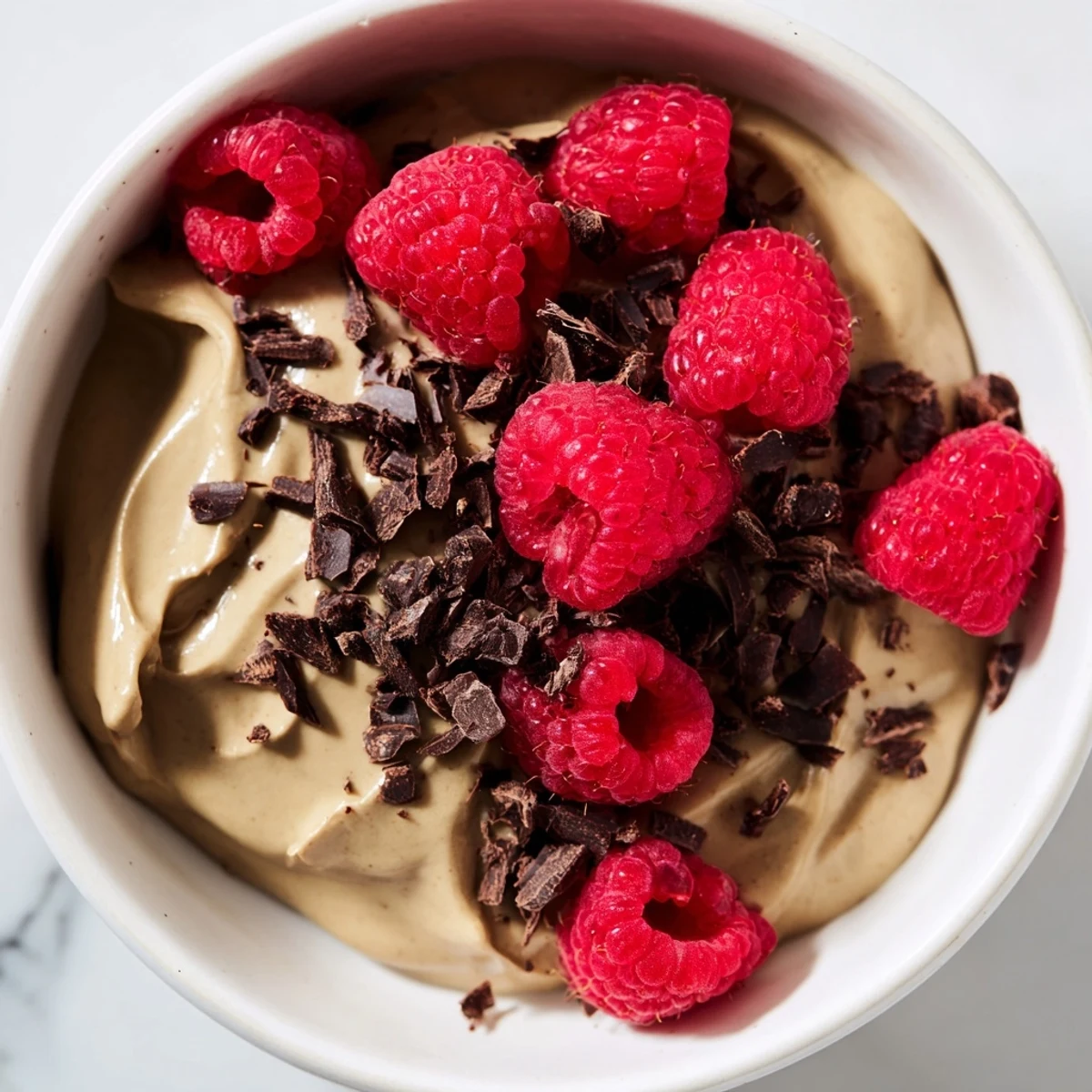 Smooth, dark Avocado Chocolate Mousse topped with vibrant red fresh raspberries, a stunning dessert.