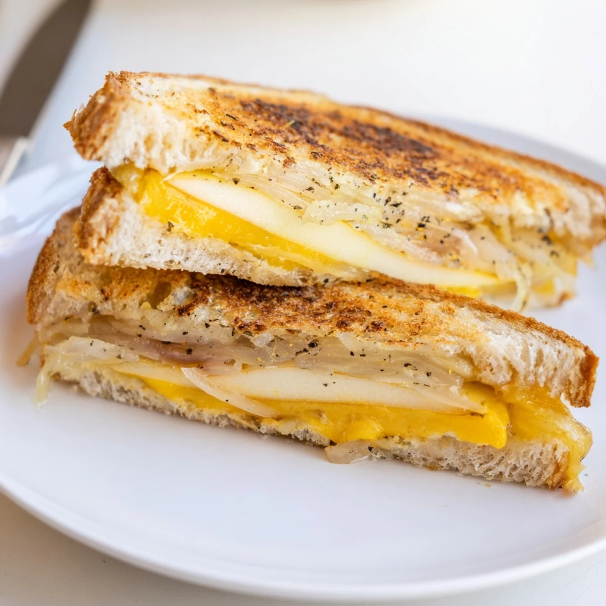 Crisp apple slices peek from bubbly, golden-brown Caramelized Onion, Apple & Cheddar Grilled Cheese sandwiches.