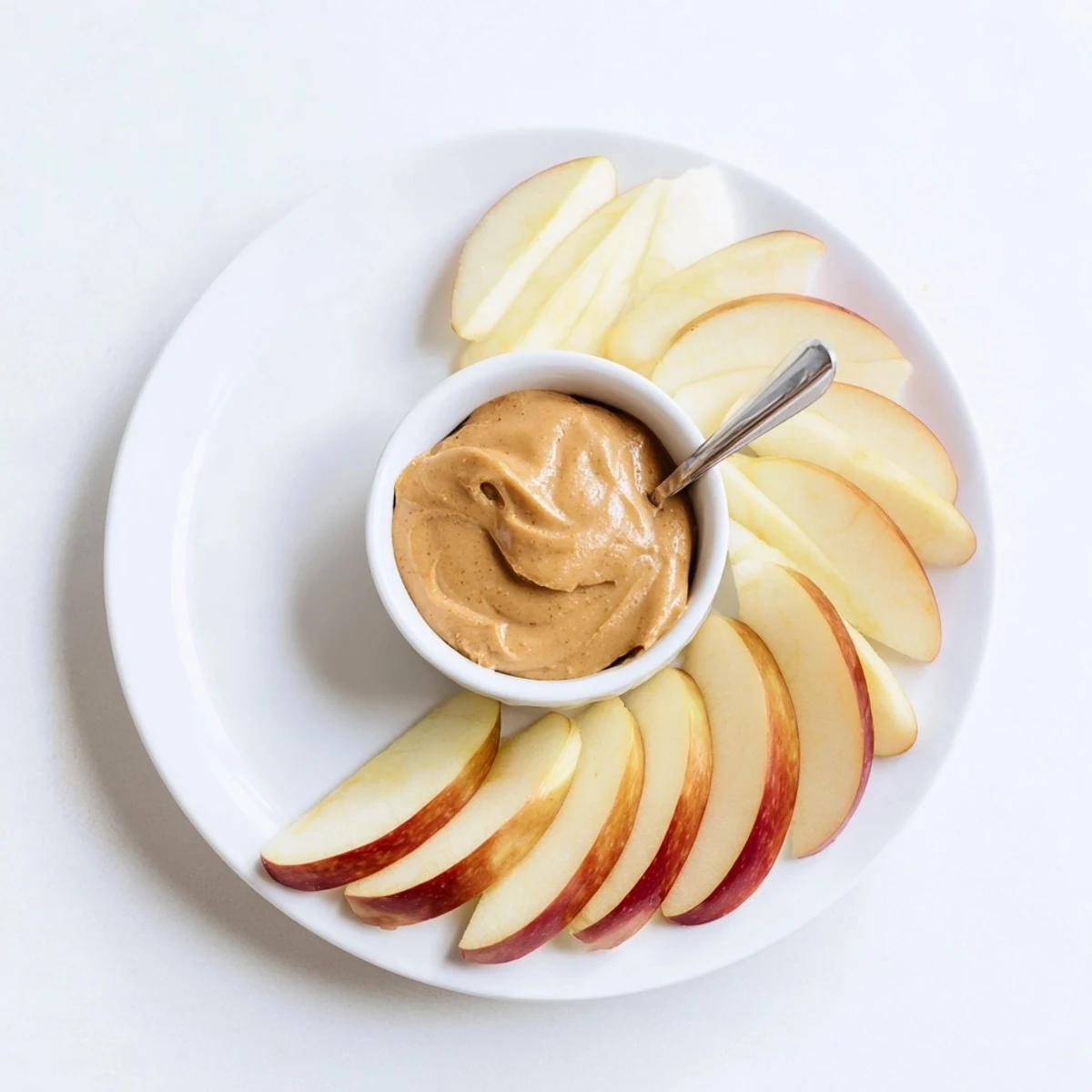 A plate of apple slices sits next to a small bowl full of peanut butter dip.