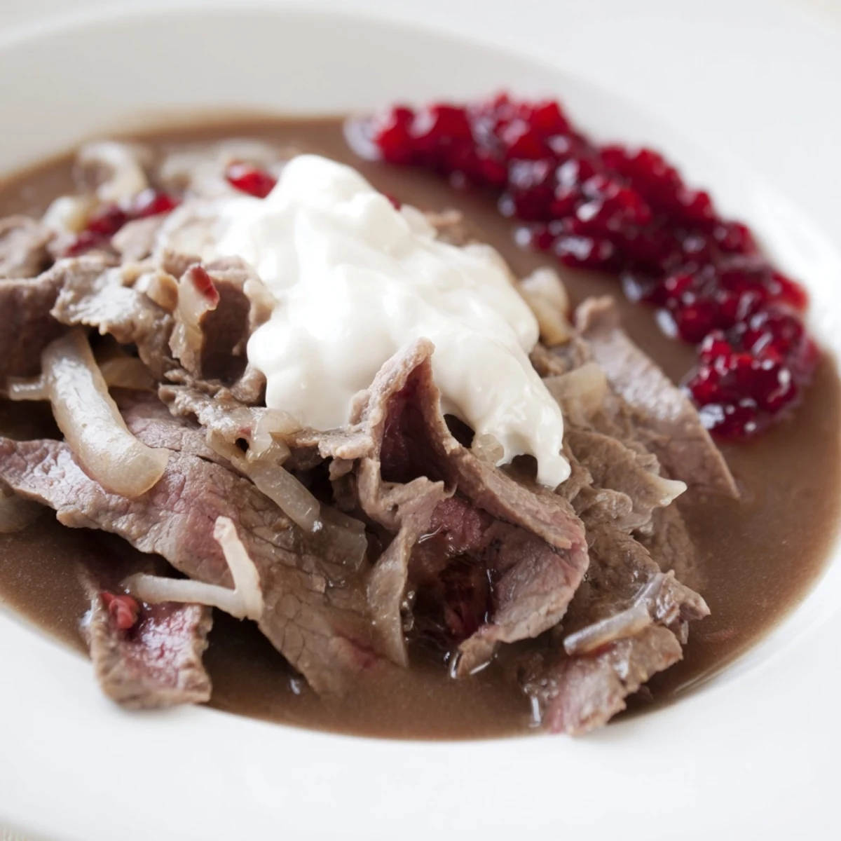 Tender Finnish Reindeer Stew, served with creamy mashed potatoes and vibrant lingonberries, promises a rich taste.