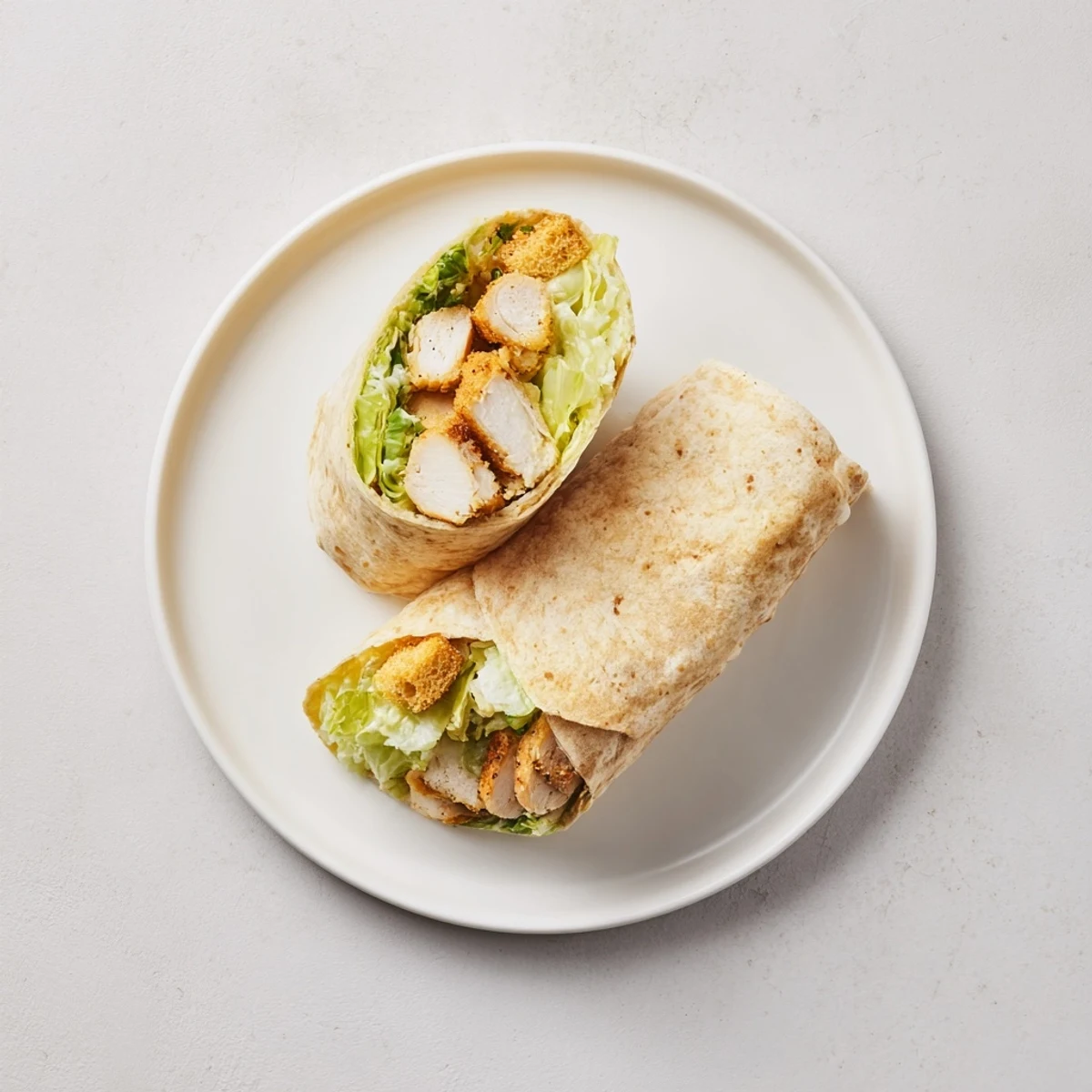 A close-up of a Caesar Chicken Salad Wrap, sliced in half to show layers of grilled chicken, crisp romaine, Caesar dressing, and parmesan on a soft tortilla.
