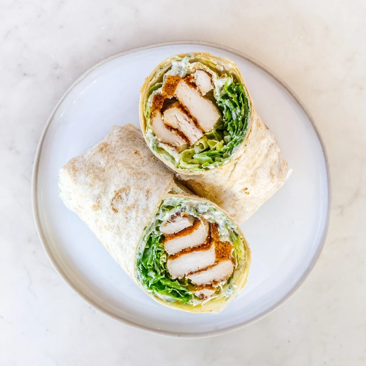 Freshly grilled Caesar Chicken Salad Wrap cut in half, revealing juicy chicken and crunchy croutons nestled in a creamy, cheesy romaine filling.