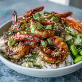 Grilled shrimp sits atop jasmine rice with crisp cucumber, carrots, and edamame in this vibrant Asian Shrimp Bowl.  