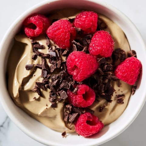 Smooth, dark Avocado Chocolate Mousse topped with vibrant red fresh raspberries, a stunning dessert.