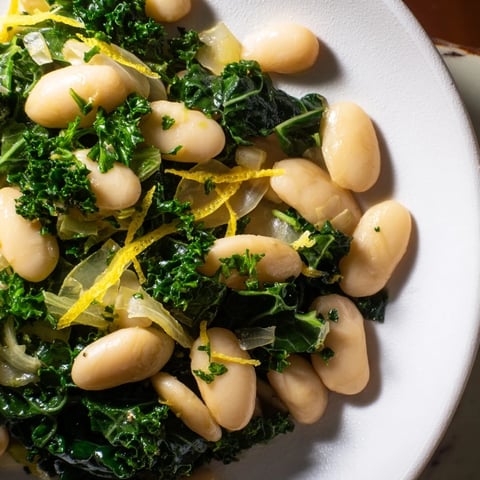 Golden, creamy Garlicky Beans with Winter Greens, served in a rustic bowl, showcasing fresh ingredients.