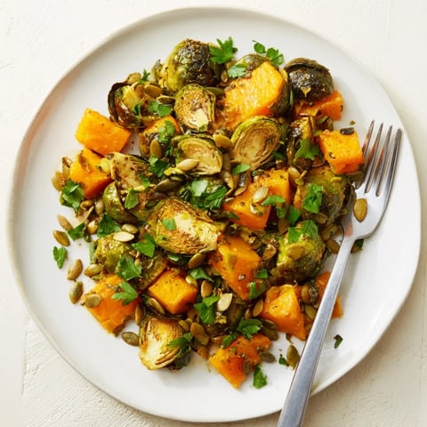 Golden-brown Roasted Brussels Sprouts & Butternut Squash, drizzled with vibrant orange dressing, is ready to serve.