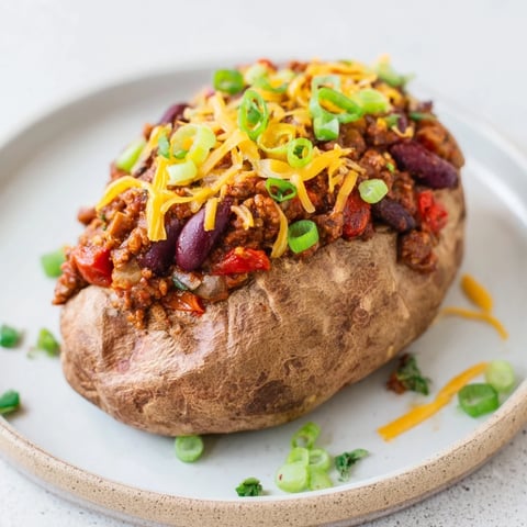 Steaming Chili-Style Baked Potatoes, loaded with a rich and flavorful bean chili and fresh toppings, ready to eat.