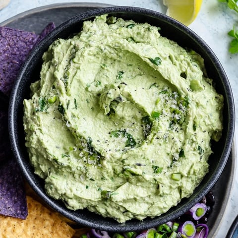 Vibrant green Witch's Brew cauldron dip surrounded by dark olives and grapes for a Halloween appetizer.