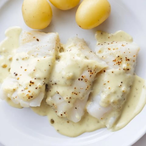 Flaky Norwegian Lutefisk, gently baked and topped with creamy mustard sauce, ready to serve.