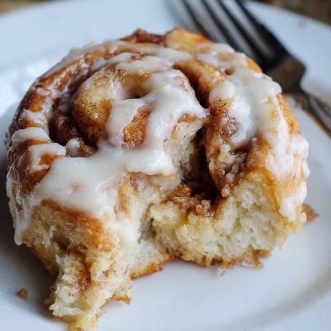 Freshly baked Pillow Soft Cinnamon Rolls with a creamy glaze, resting on a wooden serving board.