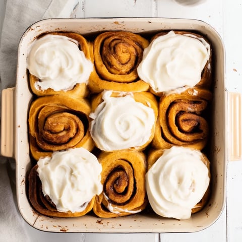 Freshly baked pumpkin cinnamon rolls cooling on a wire rack, showcasing swirls of cinnamon sugar and creamy, velvety frosting.  