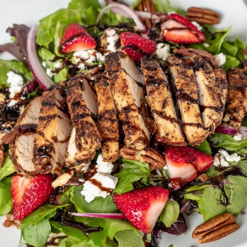 Grilled Honey Balsamic Chicken Salad with sliced strawberries, crumbled goat cheese, and mixed greens on a rustic table.