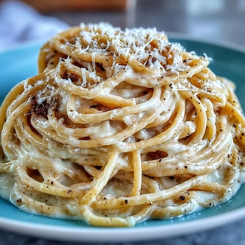 A close-up of Cacio e Pepe pasta twirled in a white bowl, flecked with freshly cracked black pepper and grated Pecorino Romano cheese.  