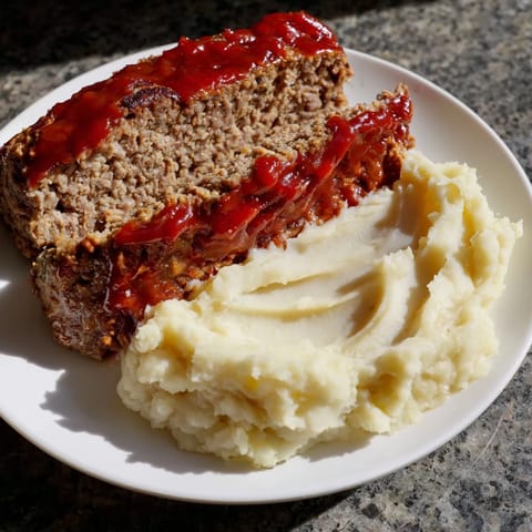 Hearty meatloaf with a glistening ketchup glaze, beside fluffy mashed potatoes, ready to be enjoyed.