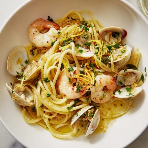 Close-up of golden shrimp and clams in Seafood Pasta Aglio e Olio with parsley garnish, ready to serve.