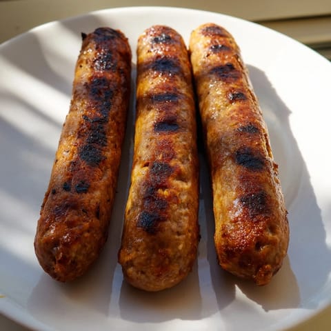 Crispy-skinned Romanian mici, flavorful ground meat rolls, being turned on a hot grill for even cooking.