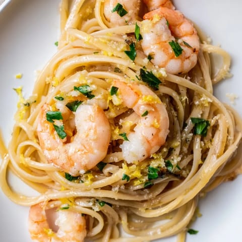 Plated Garlic Butter Shrimp Linguine garnished with lemon zest and grated Parmesan, served alongside a crisp green salad for a balanced meal.  