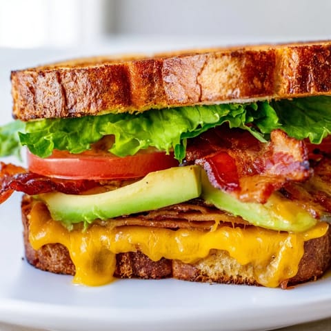 Warm Avocado BLT Grilled Cheese sandwich sliced in half, revealing creamy avocado and melted cheese on buttery sourdough.  
