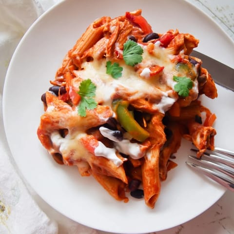 A skillet of Chicken Enchilada Pasta served hot with garnishes of cilantro, avocado, and green onions.