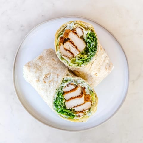 Freshly grilled Caesar Chicken Salad Wrap cut in half, revealing juicy chicken and crunchy croutons nestled in a creamy, cheesy romaine filling.