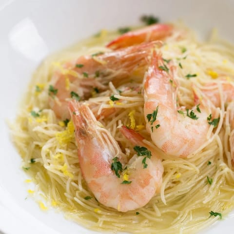 A vibrant plate of Lemon Butter Shrimp Pasta Lite features succulent shrimp tangled in angel hair pasta with a zesty lemon-garlic butter sauce and fresh parsley garnish.