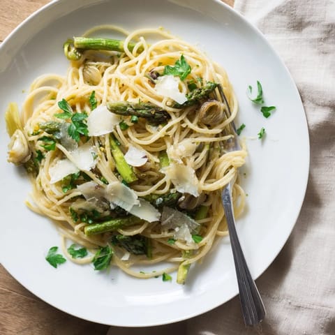 Golden roasted garlic cloves and bright green asparagus spears rest atop a bed of spaghetti, garnished with fresh parsley and Parmesan.