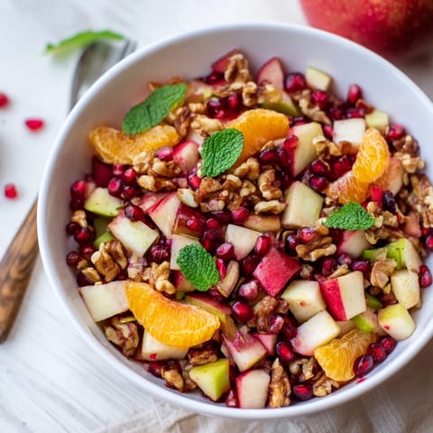 A close-up of Pomegranate and Walnut Salad glistening with a light honey-lemon dressing, garnished with fresh mint leaves on a rustic wooden table.  