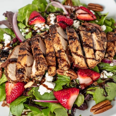 Grilled Honey Balsamic Chicken Salad with sliced strawberries, crumbled goat cheese, and mixed greens on a rustic table.