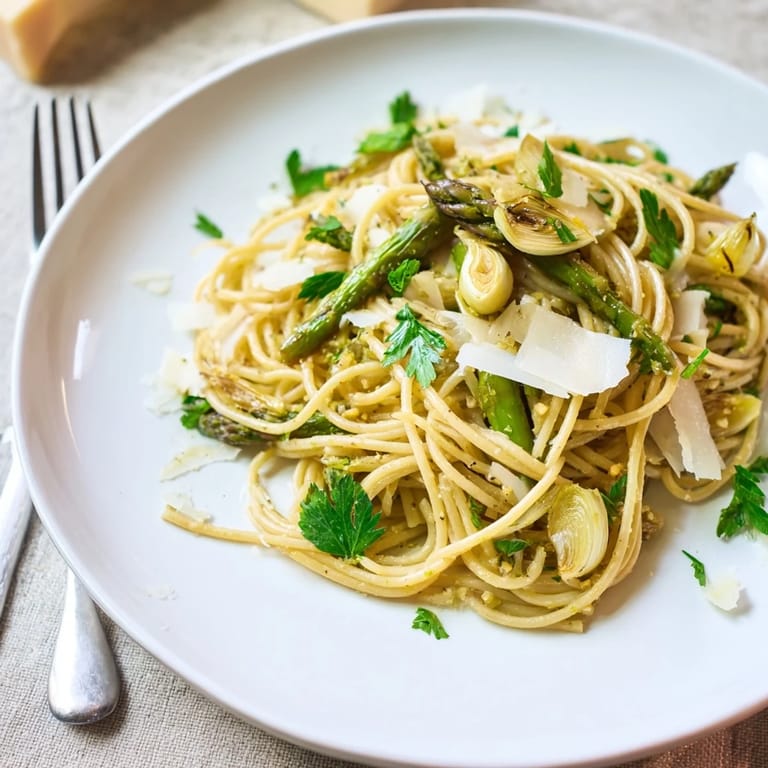 Steam rises from a skillet of Roasted Garlic & Asparagus Pasta, highlighting olive oil, roasted veggies, and grated cheese.