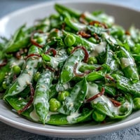 Fresh snap pea and radish salad with creamy tahini dressing, perfect for a light spring meal.